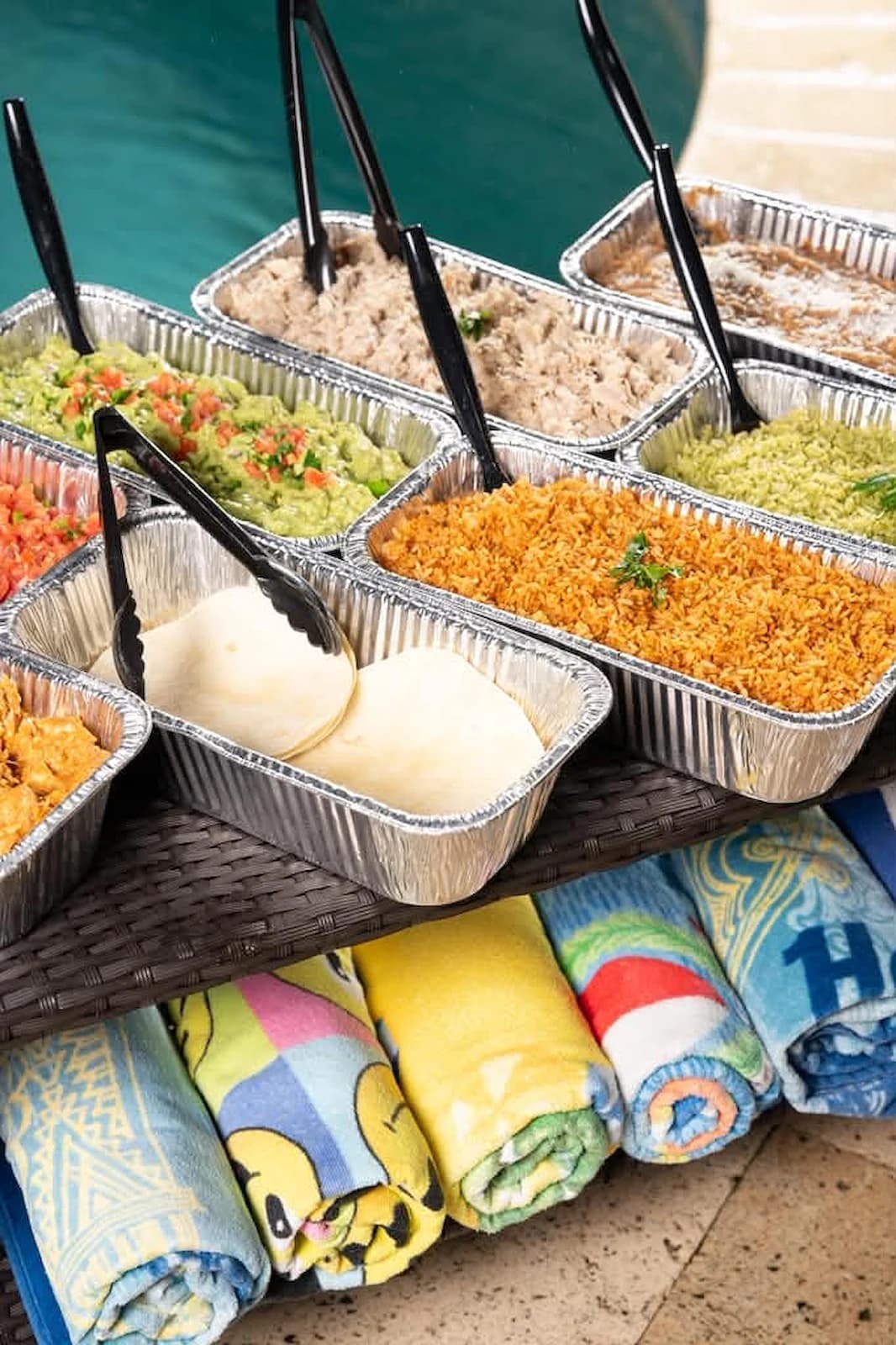 Catering trays of guacamole, pico de gallo, rice and tortillas set up by the pool
